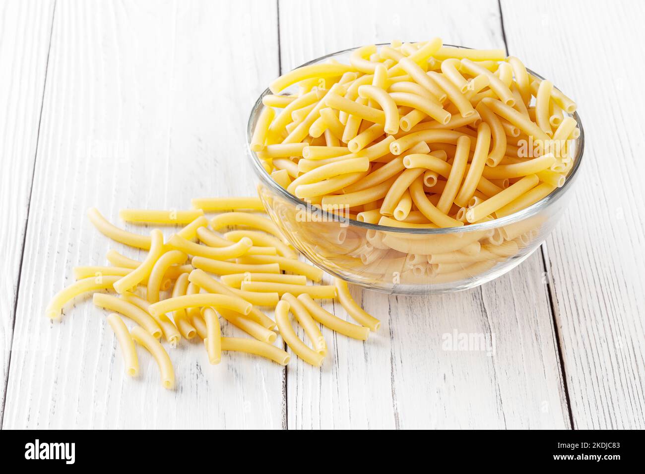 Ungekochte Makcheroni-Pasta in Glasschale auf weißem Holzhintergrund Stockfoto