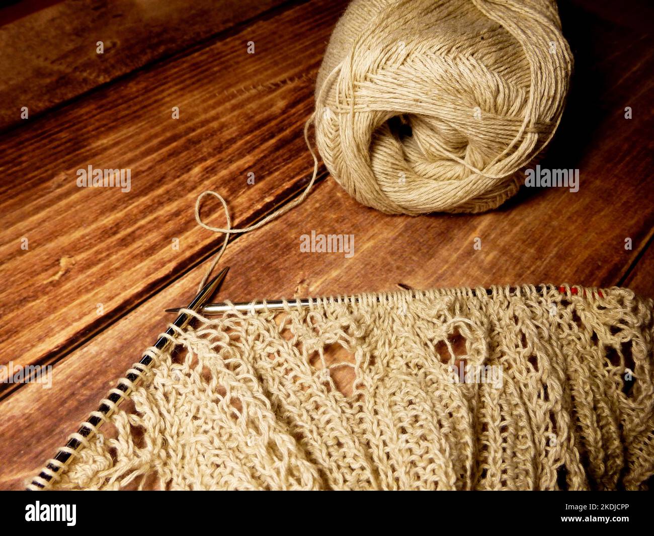 Prozess des Strickens. Stricknadeln, Schlaufen auf Stricknadeln, Strickstoff, Fadenknäuel, grobes Baumwoll- und Leinengarn, Holzhintergrund Stockfoto