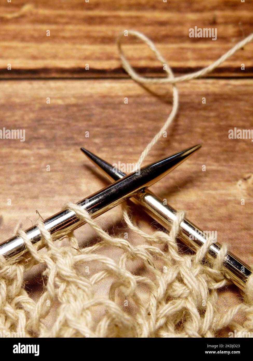 Durchbrochene Tischdecke beim Stricken. Stricknadeln, Schlaufen auf Stricknadeln, Strickstoff, grobes Baumwoll- und Leinengarn, Holzrücken Stockfoto