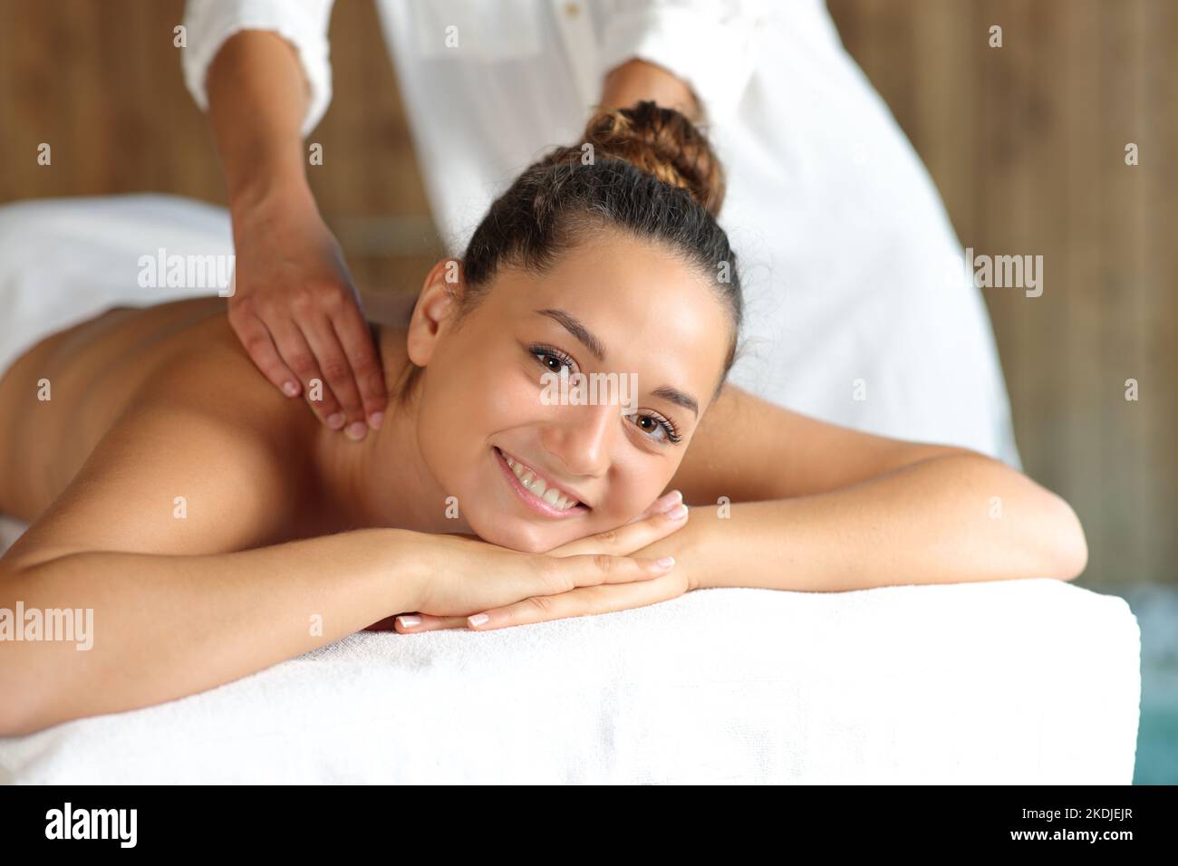 Eine glückliche Frau, die im Spa eine Massage im Rücken bekommt und dabei die Kamera anschaut Stockfoto