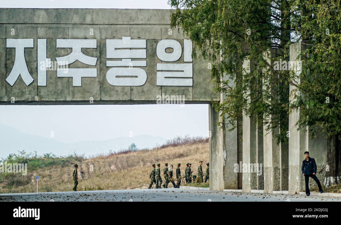 Soldaten sahen unter einem Propagandagemälde gehen, das sagte: „Lasst uns ein vereintes Mutterland übergeben!“ Am Eingang von Panmunjom von der nordkoreanischen Seite. Das Waffenstillstandsdorf Panmunjom innerhalb der entmilitarisierten Zone (DMZ) trennt Nord- und Südkorea seit 1953. Die militärische Demarkationslinie ist von Nordkoreas Seite aus zu sehen. Stockfoto