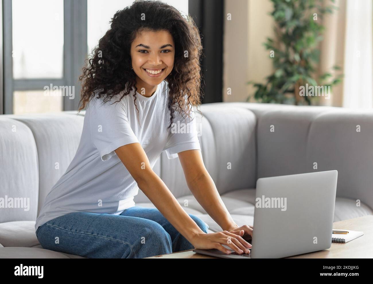 Junge afroamerikanische Frau schaut auf die Kamera und lächelt. Studentin oder Freiberuflerin, die arbeitet Stockfoto