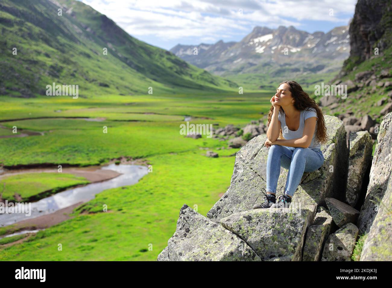 Frau, die auf einem Felsen in den Bergen sitzt und die Natur genießt, sich ausruhen und entspannen Stockfoto