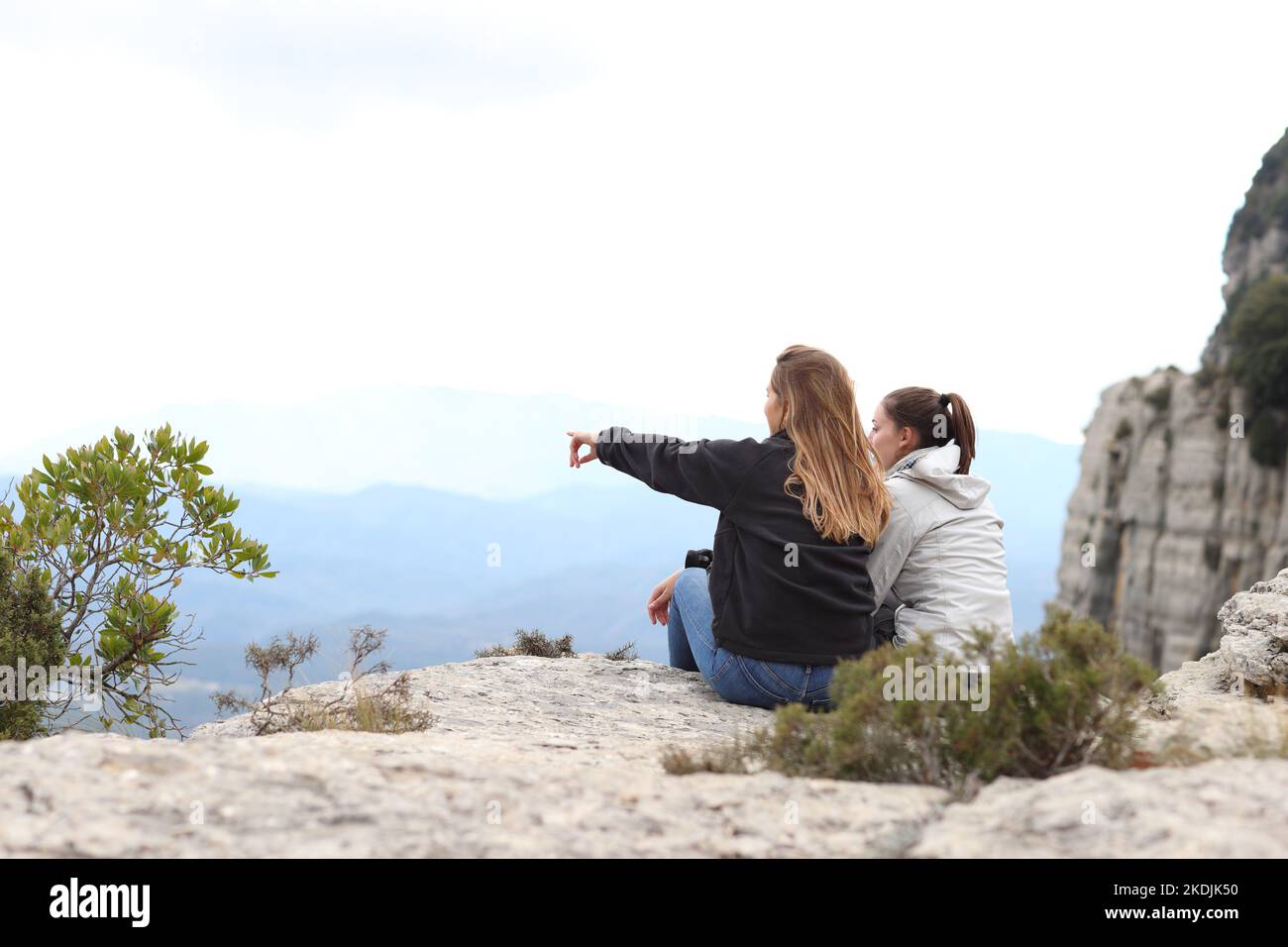 Zwei Wanderer, die die Natur betrachten, sitzen auf einer Klippe und zeigen weg Stockfoto