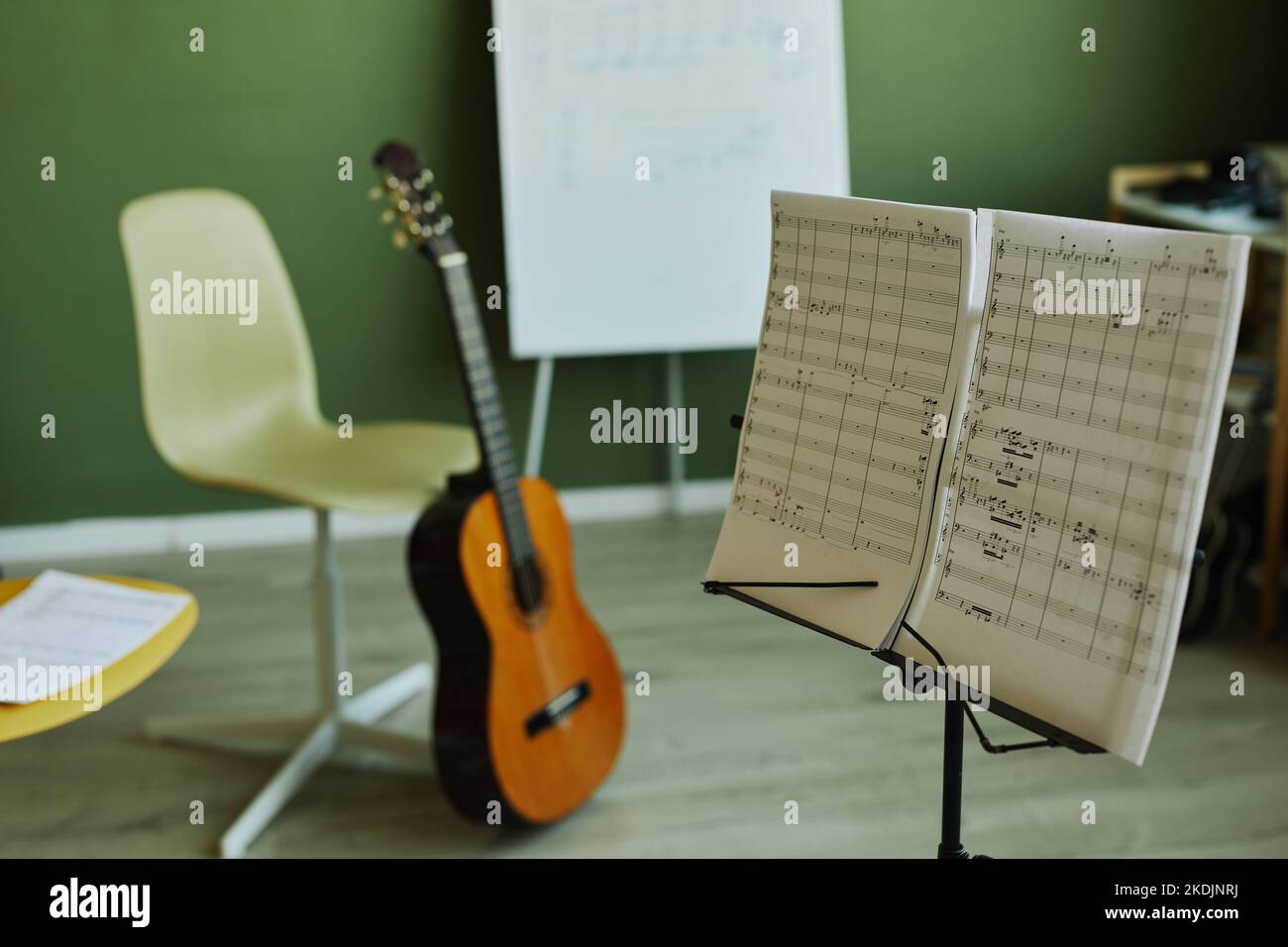 Zwei Papiere mit Musiknoten stehen auf dem Hintergrund der Gitarre, Stühle für Schüler und Whiteboard für Lehrer in geräumigen Klassenzimmern Stockfoto