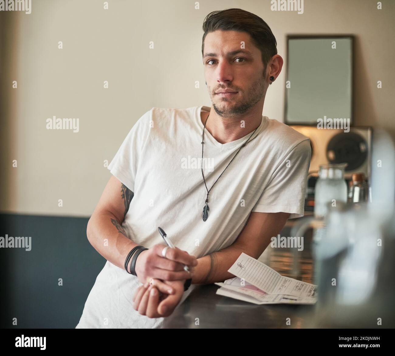 Wenn Sie es trinken können, kann er es mischen. Porträt eines ernsthaften jungen Barkeepers, der sich an der Theke lehnt. Stockfoto