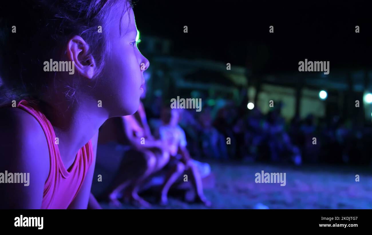 Sommer, Nacht, in den Strahlen der Soffits, ein Mädchen von sieben Jahren, beobachten das Nachtkonzert in einem Open-Air-Theater, im Urlaub. Viele Kinder sind im Hintergrund. Hochwertige Fotos Stockfoto