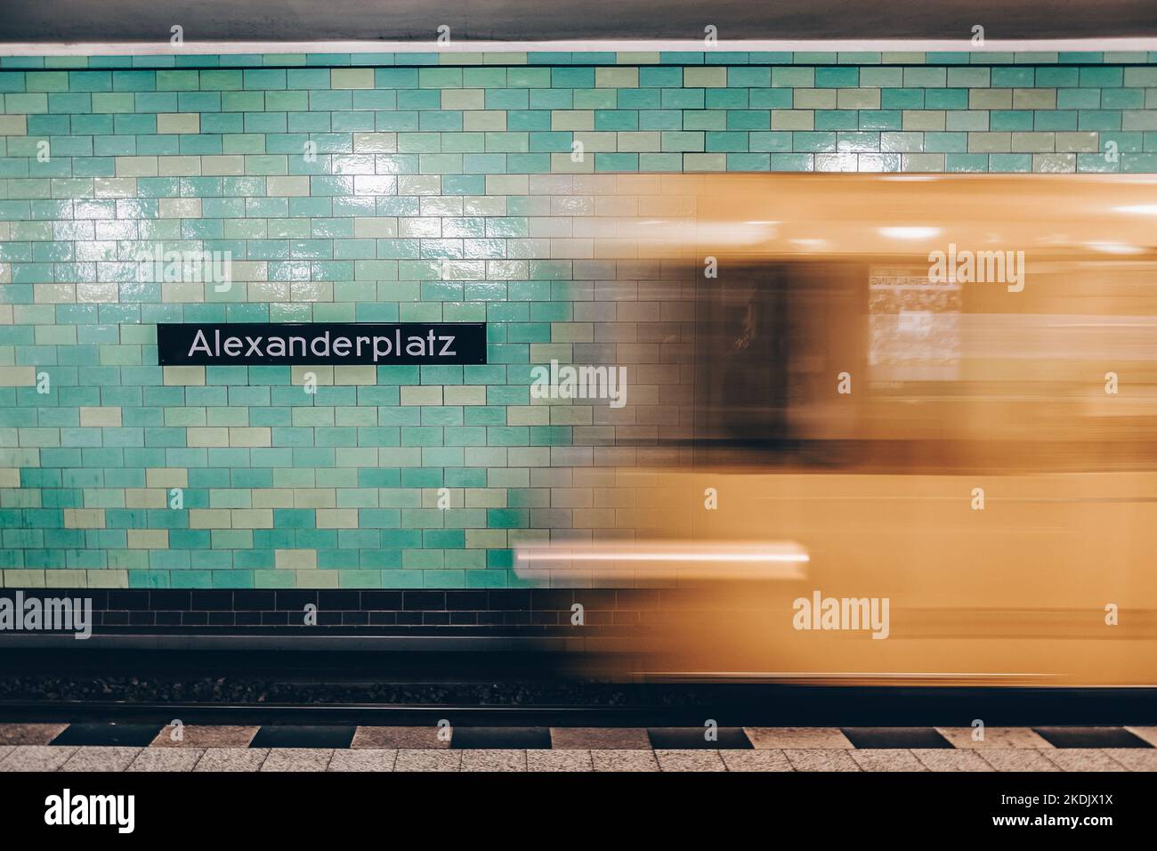 Gelbe U-Bahn Zug in Bewegung. Berlin Alexanderplatz Zeichen sichtbar an der Wand der U-Bahnstation. Stockfoto