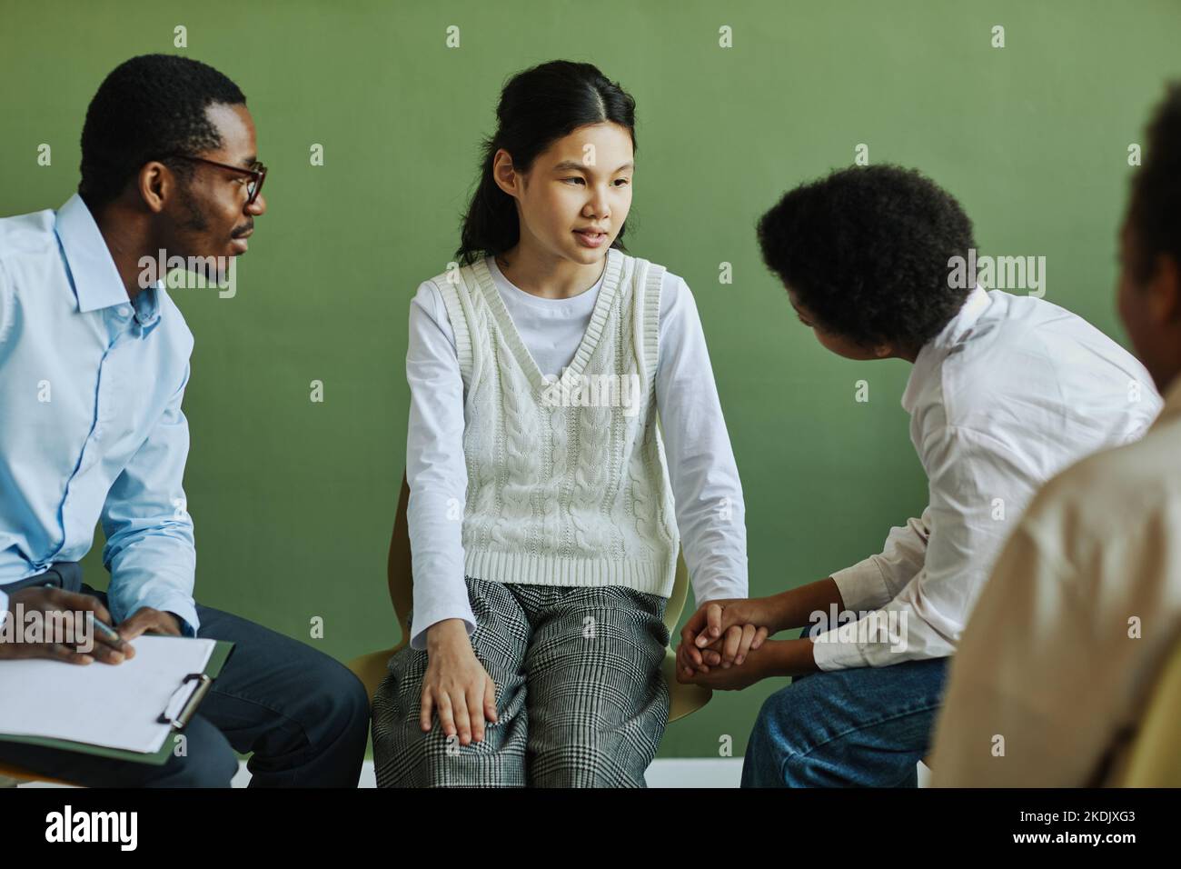 Jugendliches Schulmädchen im Gespräch mit dem Schuljungen, der ihre Hände während der Diskussion über ihre Probleme in einer psychologischen Sitzung hält Stockfoto