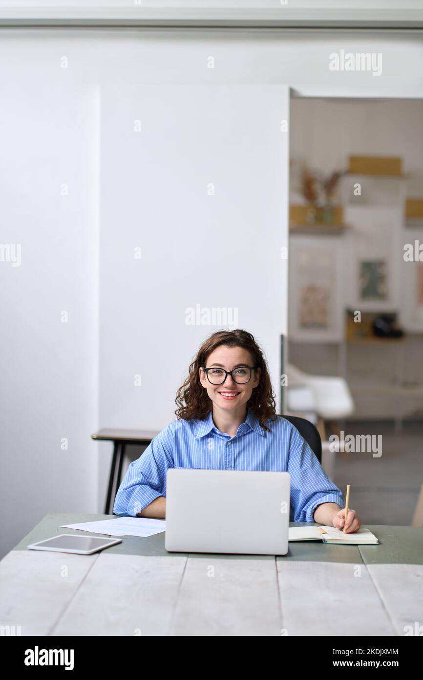 Junge glückliche Geschäftsfrau Student sitzt am Schreibtisch mit Laptop. Hochformat Stockfoto