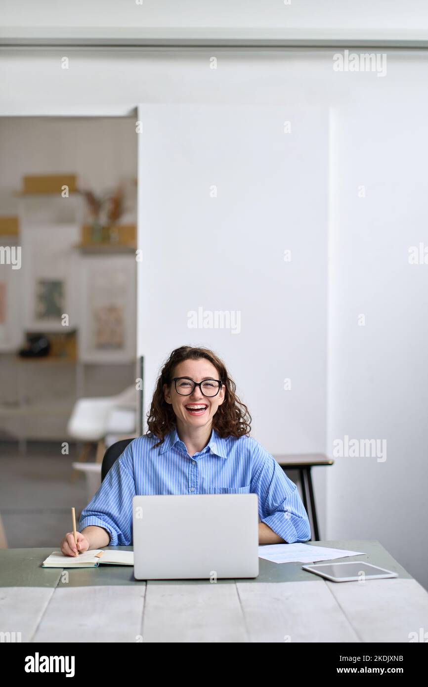 Junge, fröhliche Geschäftsfrau, Studentin, die mit einem Laptop am Schreibtisch sitzt. Stockfoto