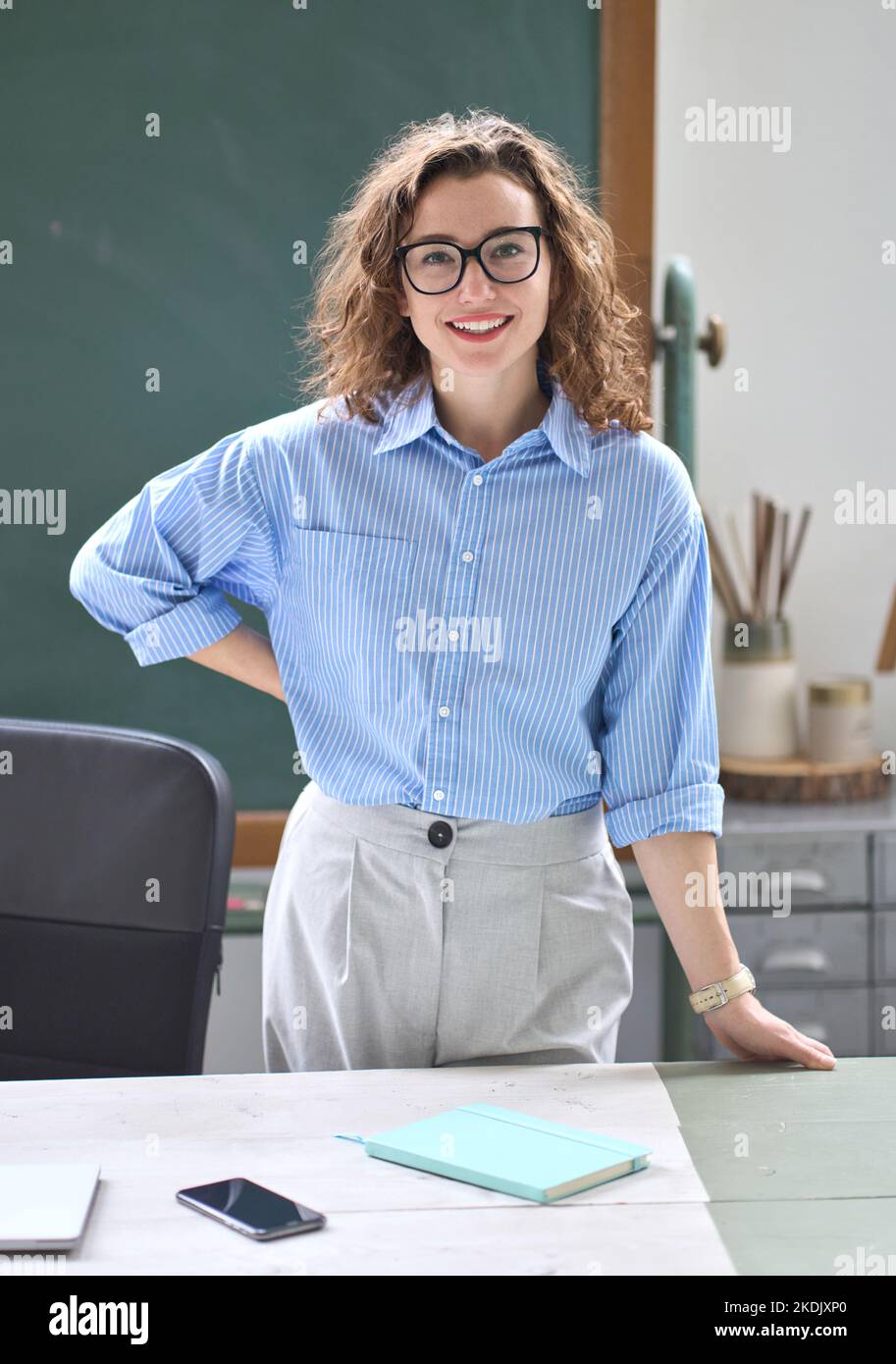 Junge glückliche Frau Lehrer Coach steht am Schreibtisch im Klassenzimmer Büro. Hochformat Stockfoto