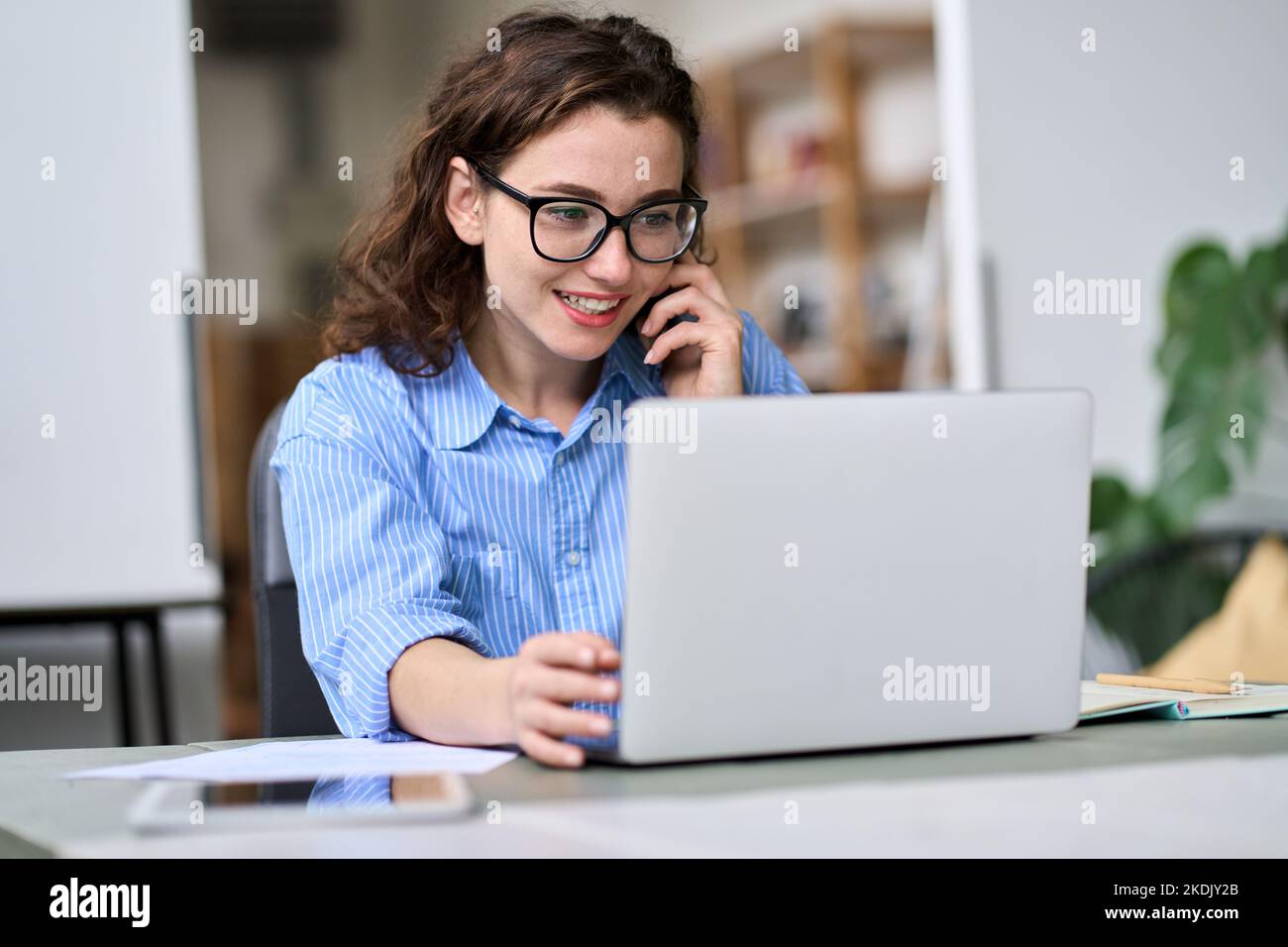 Junge Frau, die mit einem Laptop telefoniert und online arbeitet. Stockfoto