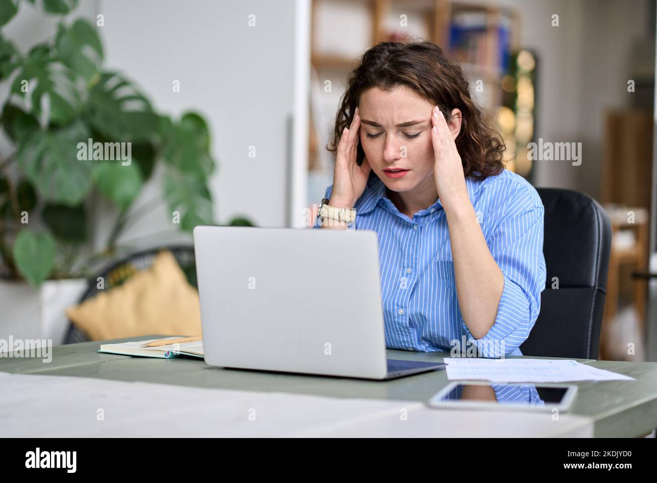 Gestresste junge Angestellte, die den Kopf berührt und Kopfschmerzen fühlt, Müdigkeit bei der Arbeit. Stockfoto