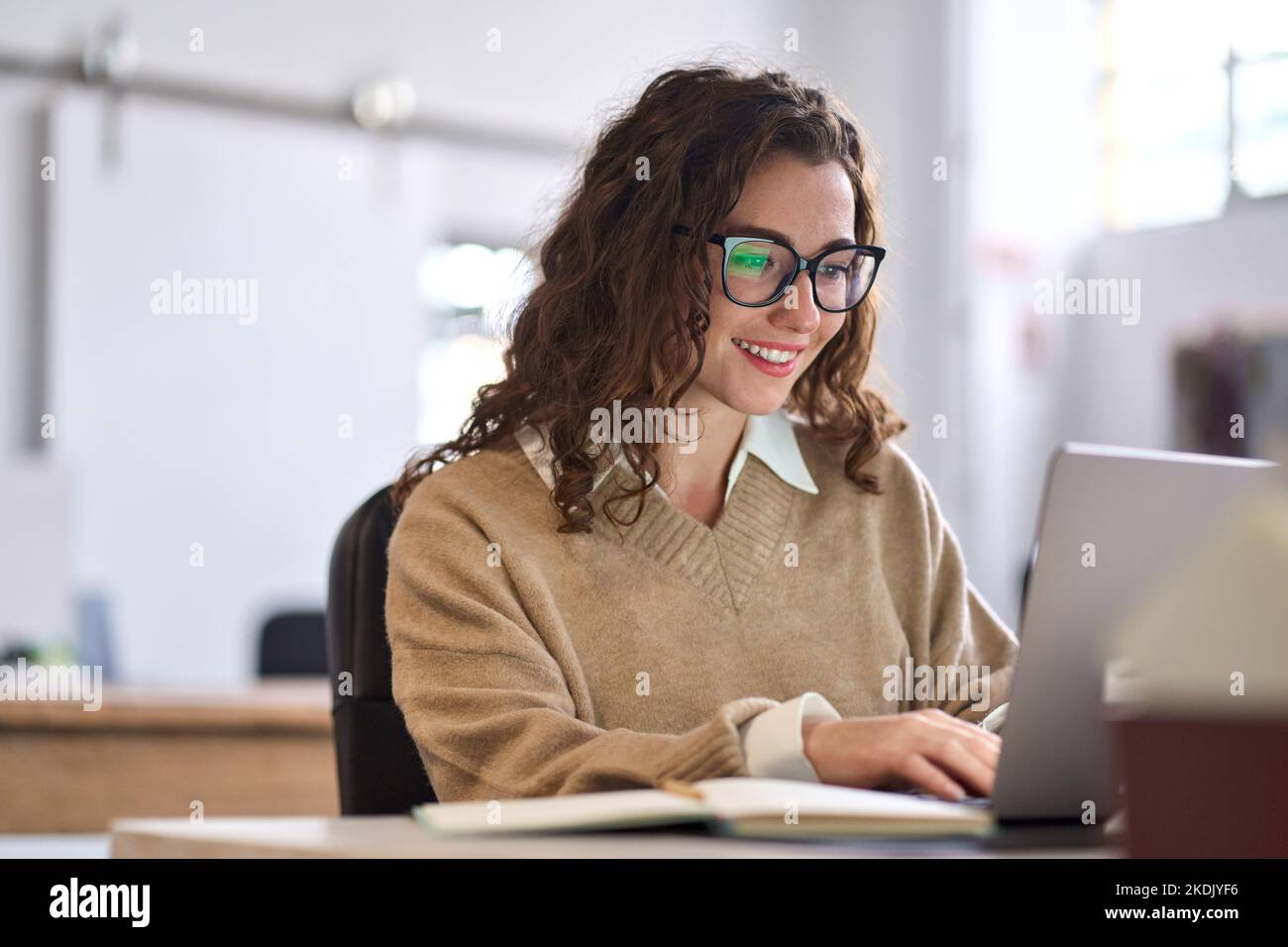 Junge glückliche Angestellte oder Studentin, die mit einem Laptop am Schreibtisch sitzt. Stockfoto