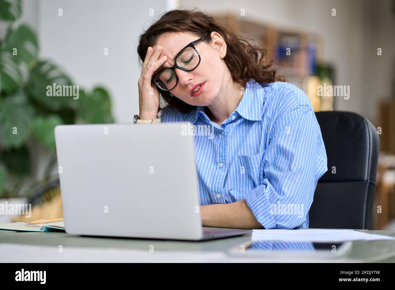 Müde junge Geschäftsfrau berühren Kopf Gefühl Kopfschmerzen Migräne mit Laptop. Stockfoto