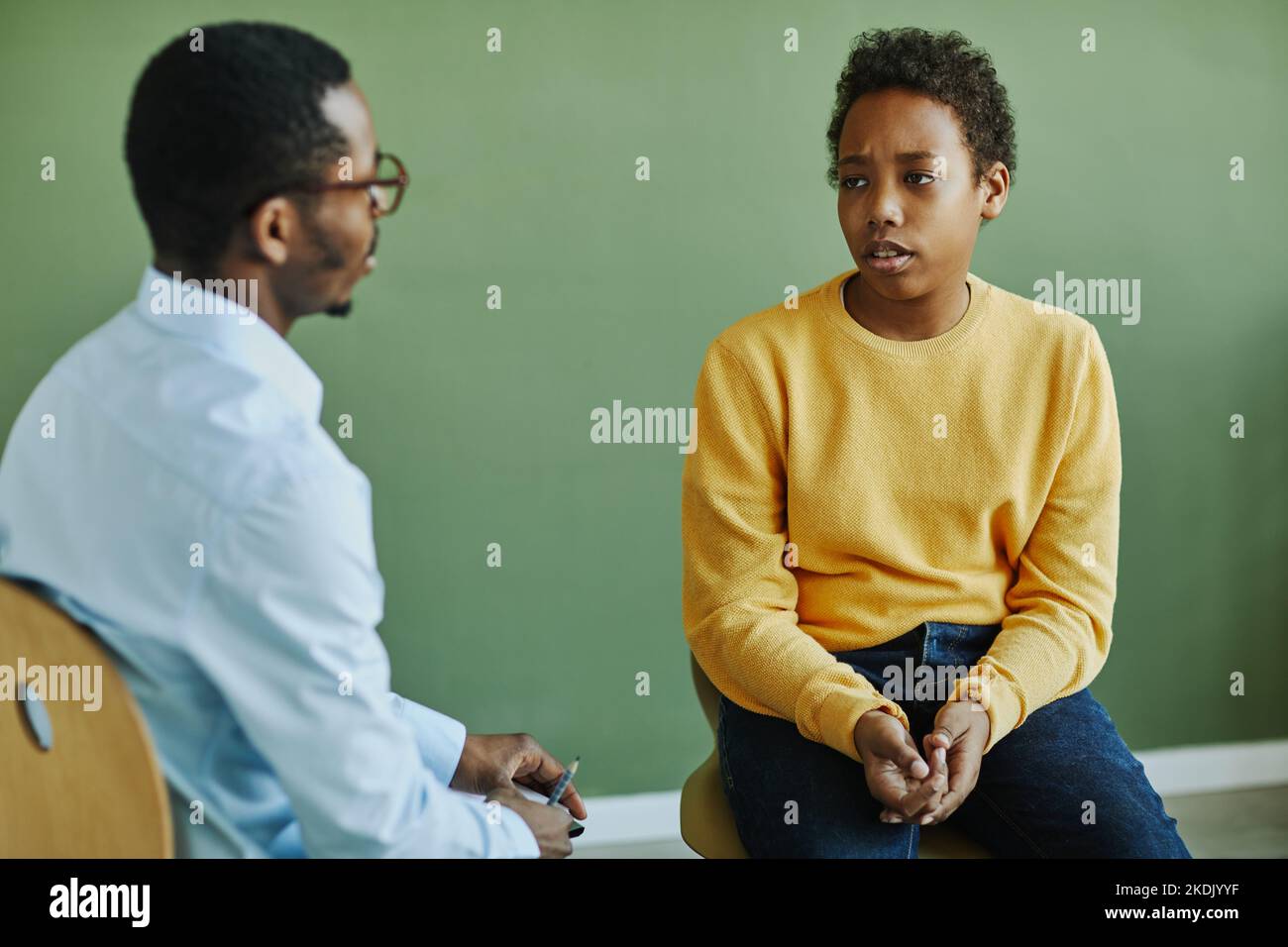 Verärgert Schuljunge in Casualwear beschreibt sein Problem an junge afroamerikanische Schulpsychologe während der Einzelsitzung nach dem Unterricht Stockfoto