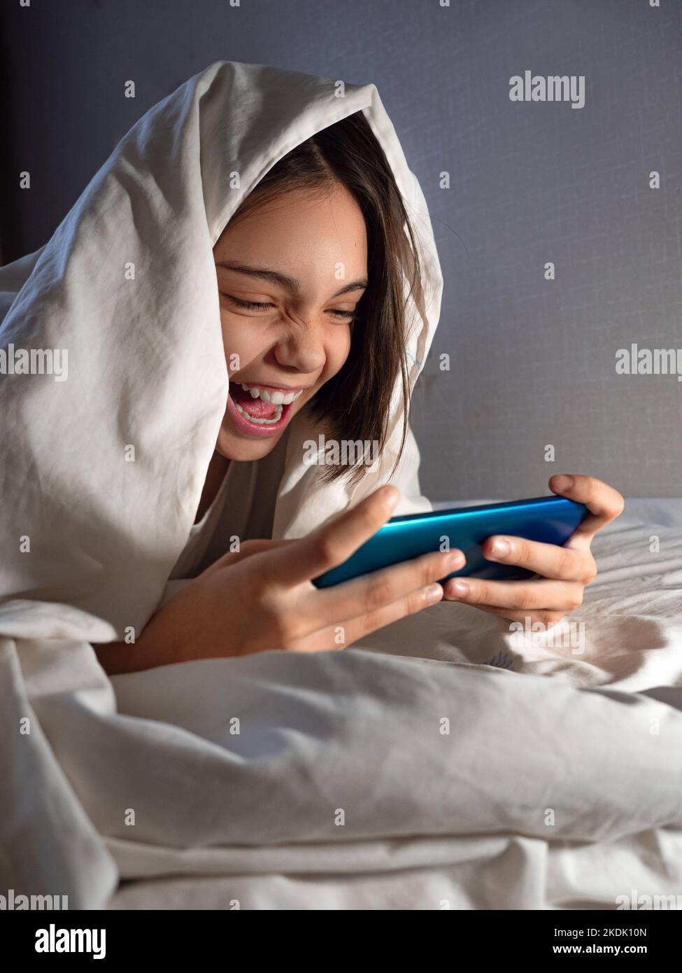 Teenager-Mädchen spielt nachts mit ihrem Smartphone im Bett unter der Decke. Smartphone- und Gaming-sucht-Konzept. Stockfoto