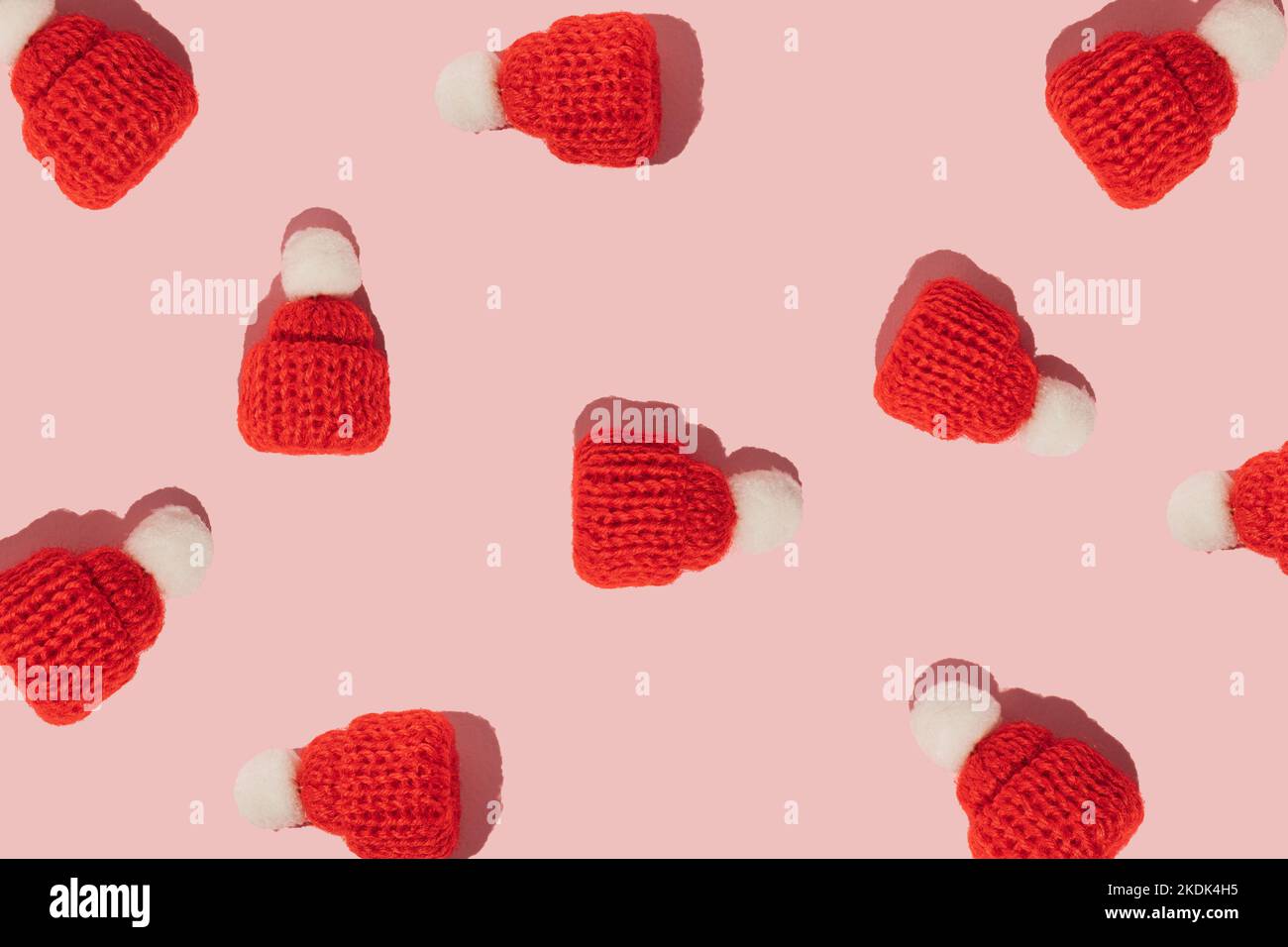 Weihnachtsgruß-Muster mit roten Wintermützen auf rosa Hintergrund. Minimalkonzept. Stockfoto