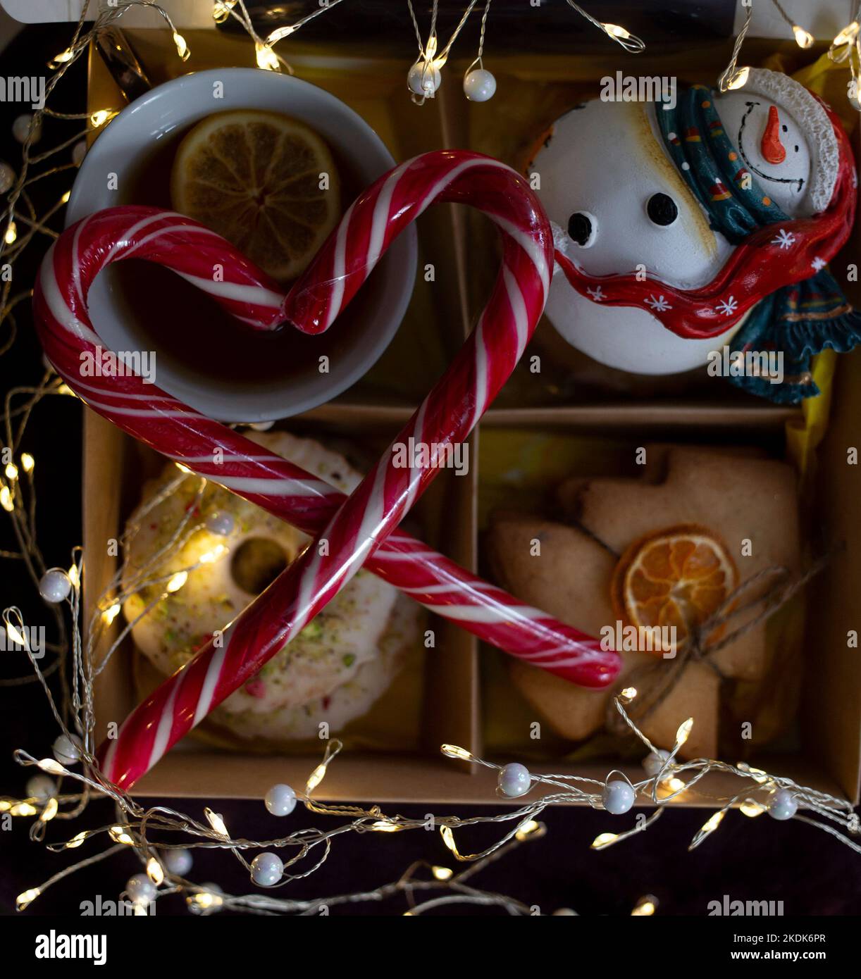 Gemütliche leckere stimmungsvolle Foto über Neujahr Thema. tasse mit Tee, Zitronenscheiben, Lebkuchen, Schneemann, leuchtende Girlanden, Lutscher in s gefaltet Stockfoto