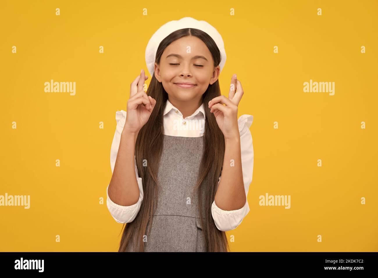 Lustiges Teenager-Kind, das die Daumen für Viel Glück. drückt Mädchen betet und hofft, dass Träume wahr werden, isoliert auf gelbem Hintergrund. Stockfoto