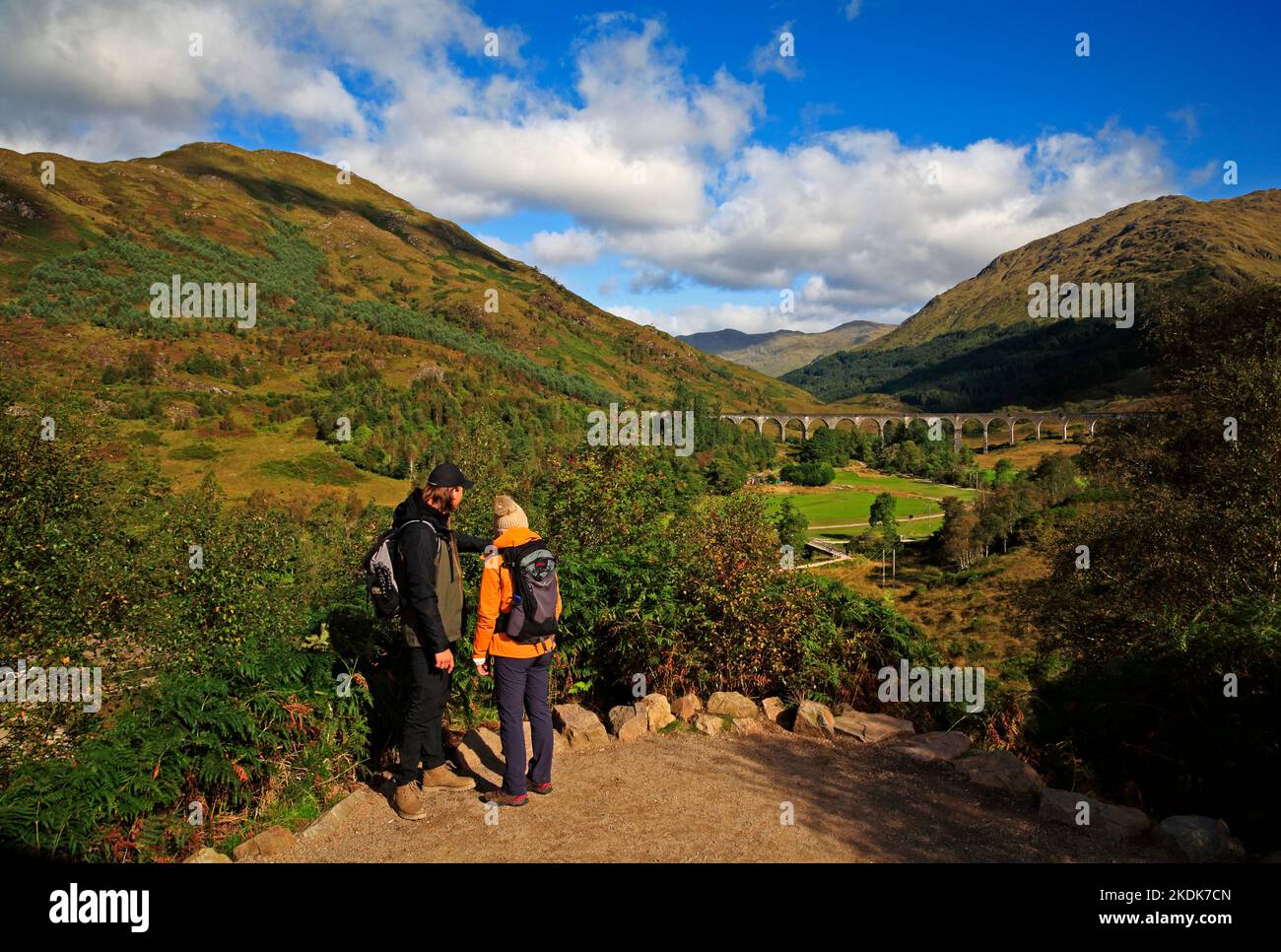 Zwei junge Menschen stehen auf einem Aussichtspunkt mit Blick auf das Glenfinnan Viadukt und Glen Finnan in den Highlands in Glenfinnan, Lochaber, Schottland. Stockfoto