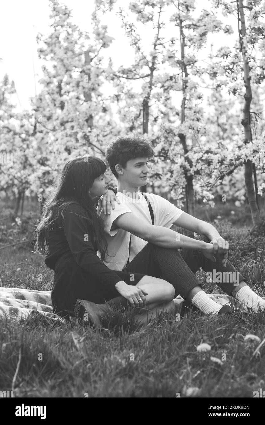 Das schöne junge Paar erklärt in einem blühenden Apfelgarten mit einem Lächeln auf den Gesichtern ihre Zuneigung, Zweisamkeit und Liebe. Echtes Paar in Schwarz Stockfoto