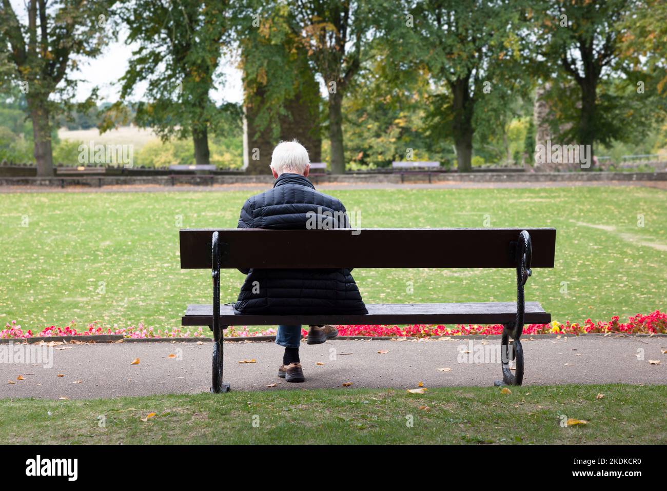 KNARESBOROUGH, Großbritannien - 20. September 2022. Älterer Mann mit grauen Haaren sitzt allein auf einer Parkbank im Herbst. Knaresborough, Yorkshire, Großbritannien Stockfoto