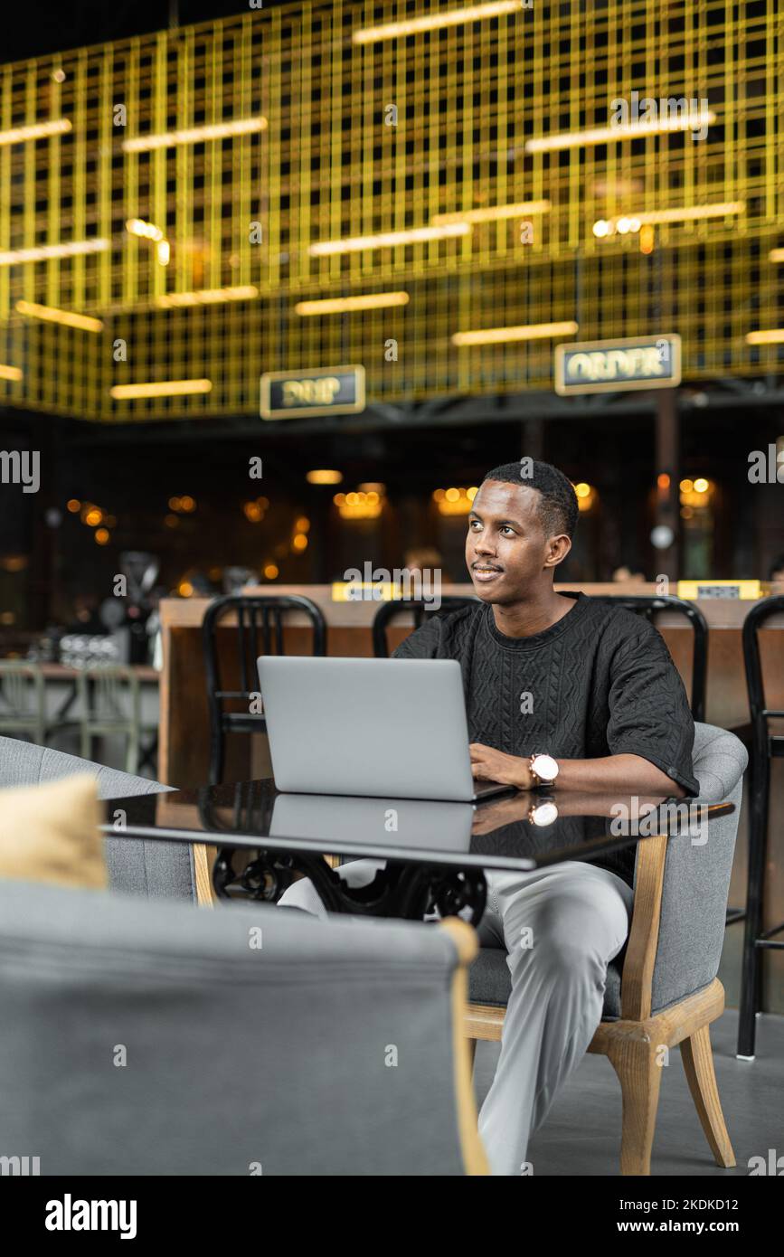 Porträt eines hübschen jungen schwarzen Mannes, der im Café einen Laptop verwendet Stockfoto
