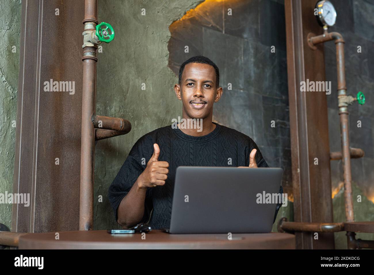Porträt eines hübschen schwarzen Mannes, der in Innenräumen sitzt und einen Laptop benutzt Stockfoto