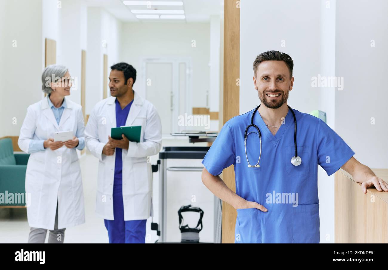 Lächelndes Pflegepersonal in blauer Uniform mit Stethoskop vor dem Krankenhauskorridor. Medizinisches Personal Stockfoto