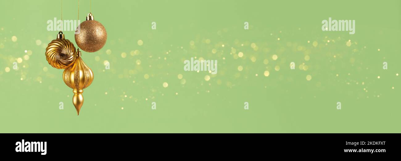 Weihnachtsbanner mit drei goldenen Kugeln Dekorationen auf grünem Hintergrund mit Bokeh-Lichtern mit Kopierraum. Weitwinkelvorsatz Stockfoto