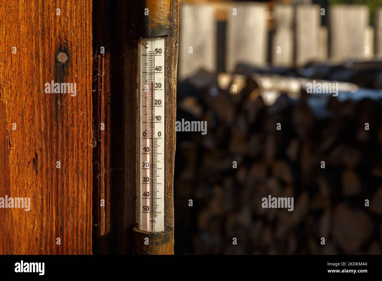Outdoor-Thermometer an der Wand des Hauses. Thermometer, das an einer Holzwand in der Straße hängt. Sommerhitze, Celsius-Skala Stockfoto