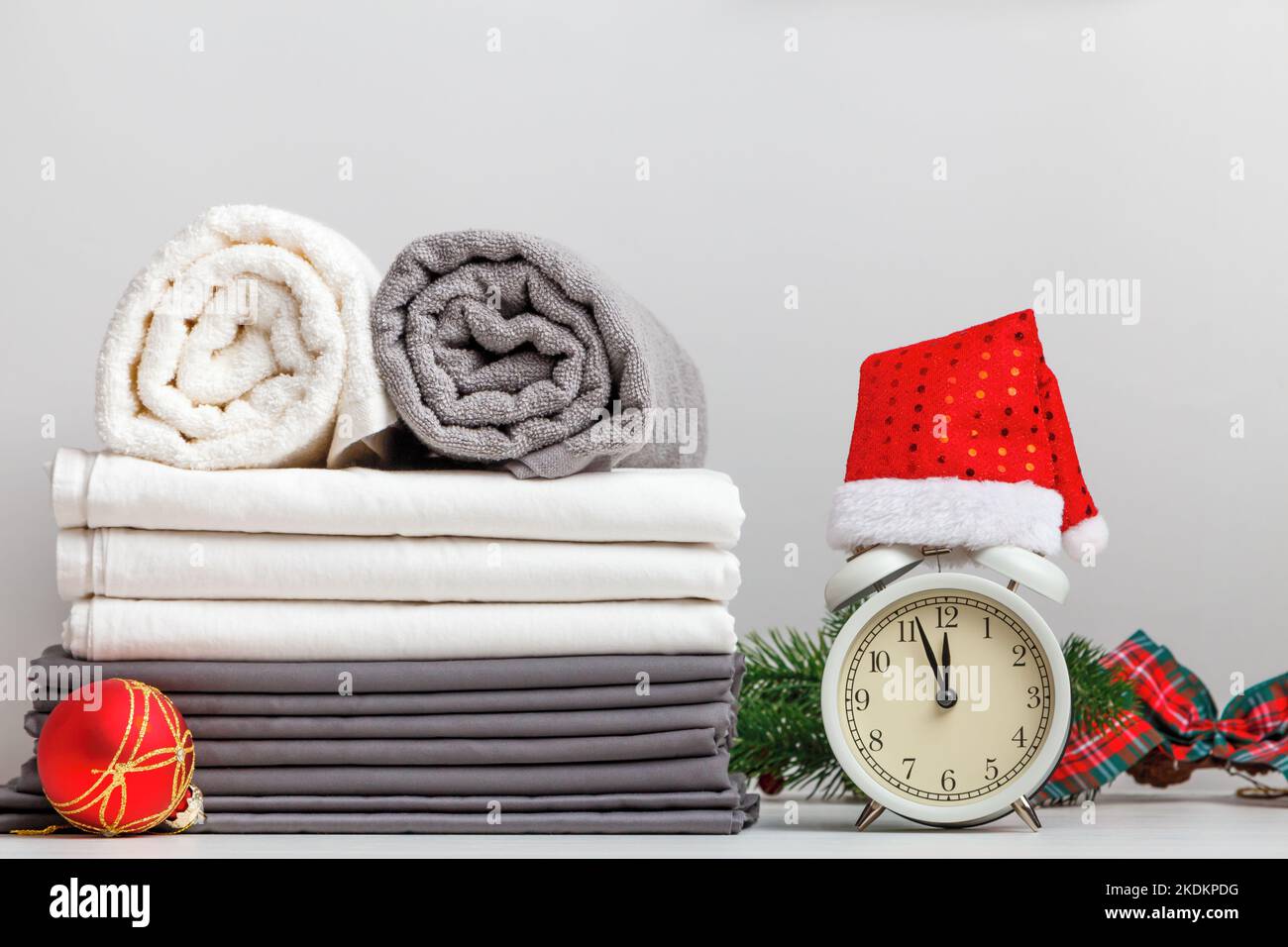 Stapel gefalteter Handtücherrollen und Bettwäsche, Laken auf dem Tisch mit weihnachtlicher Einrichtung und Wecker Stockfoto
