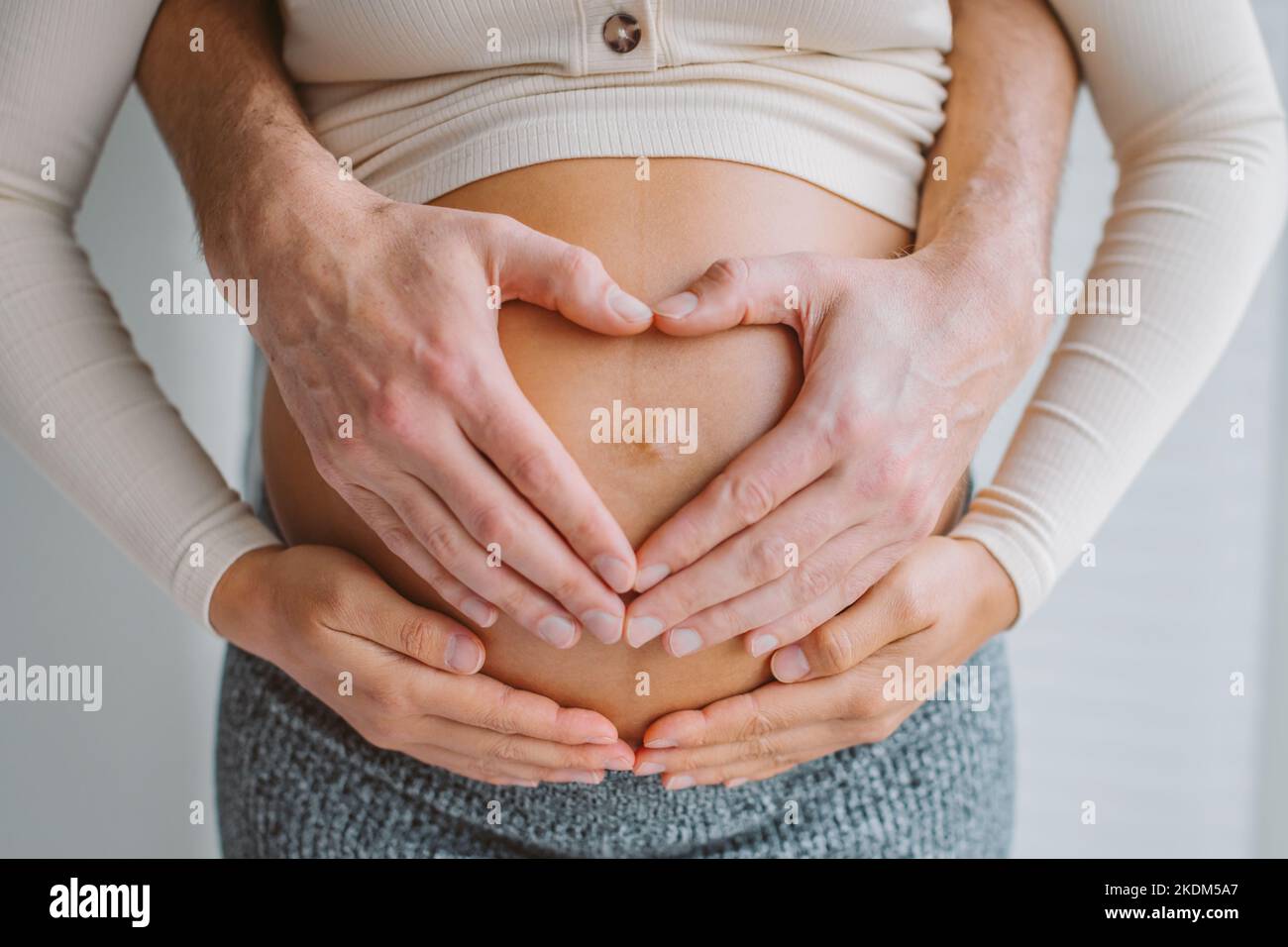 Liebevolle Eltern Herz Form Hände auf schwanger Frau Bauch. Erwartet Paar in der Liebe Schwangerschaft Nahaufnahme Foto des Bauches. Stockfoto