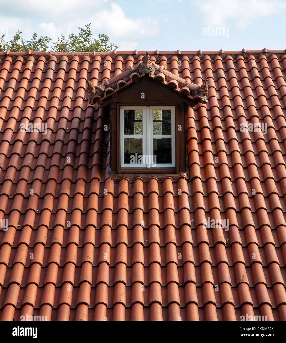 Rotes Ziegeldach mit Dachboden. Dachfenster weiß auf Dachboden. Wolkiger Himmel im Hintergrund. Stockfoto