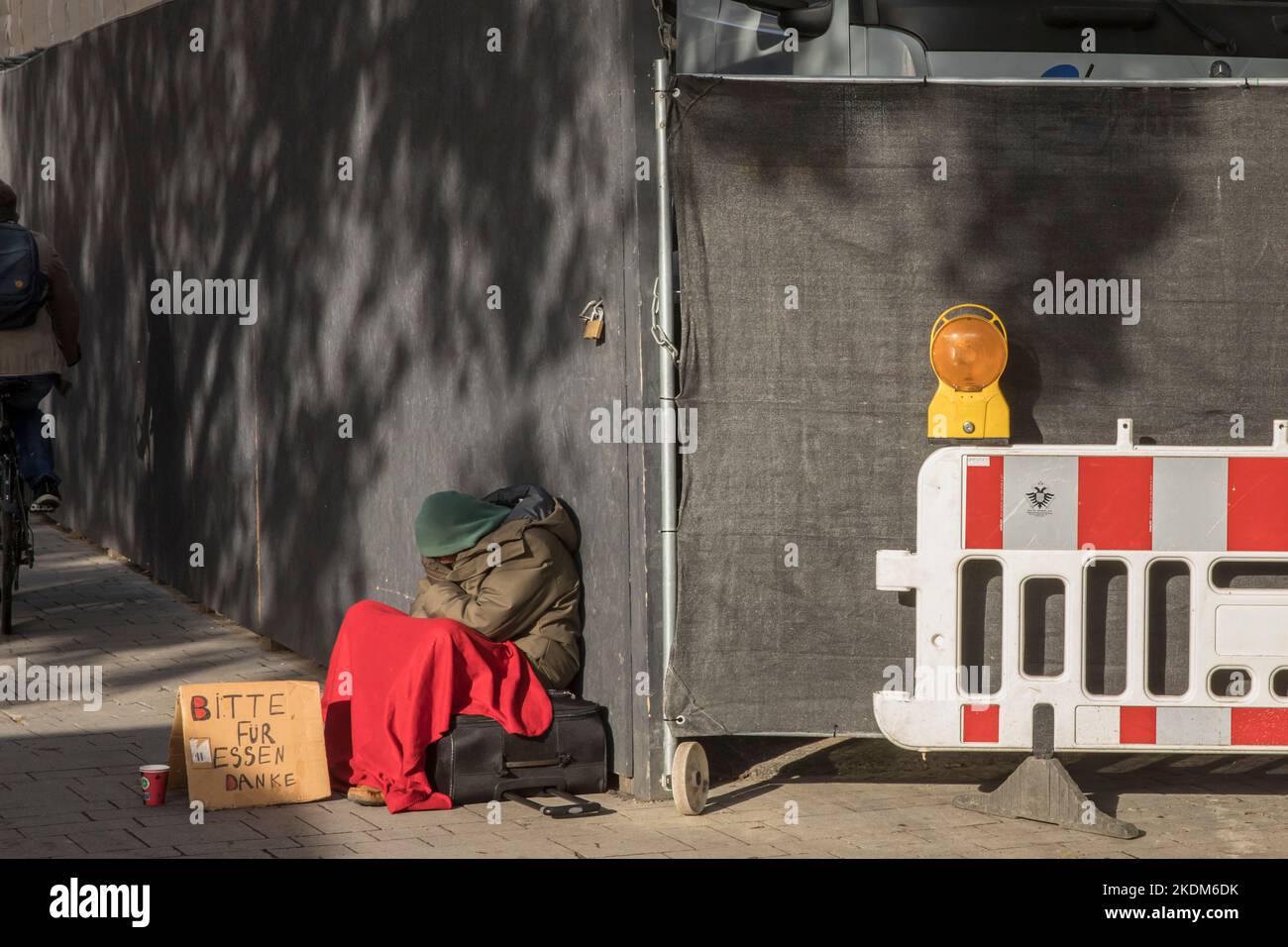 Bettler, der vor einem Bauzaun in der Nähe des Kölner Doms sitzt. Bettler sitzt vor einem Bauzaun nahe Dom, Köln, Deutschland. Stockfoto