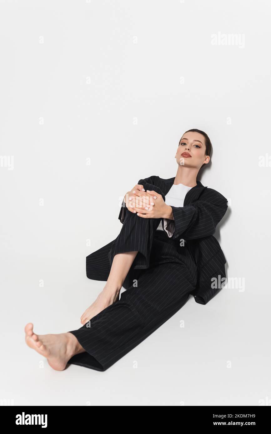 In voller Länge modische Modell in Anzug berühren Knie auf weißem Hintergrund Stockfoto