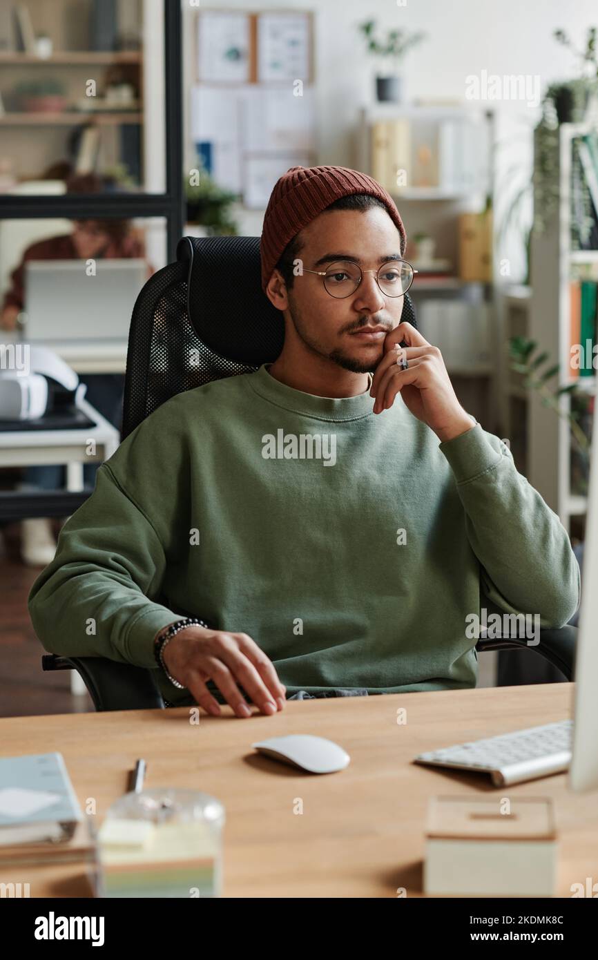 Ein junger moderner IT-Ingenieur sitzt am Arbeitsplatz vor dem Computer und schaut auf den Bildschirm, während er ein neues Programm zur Entschlüsselung von Informationen startet Stockfoto