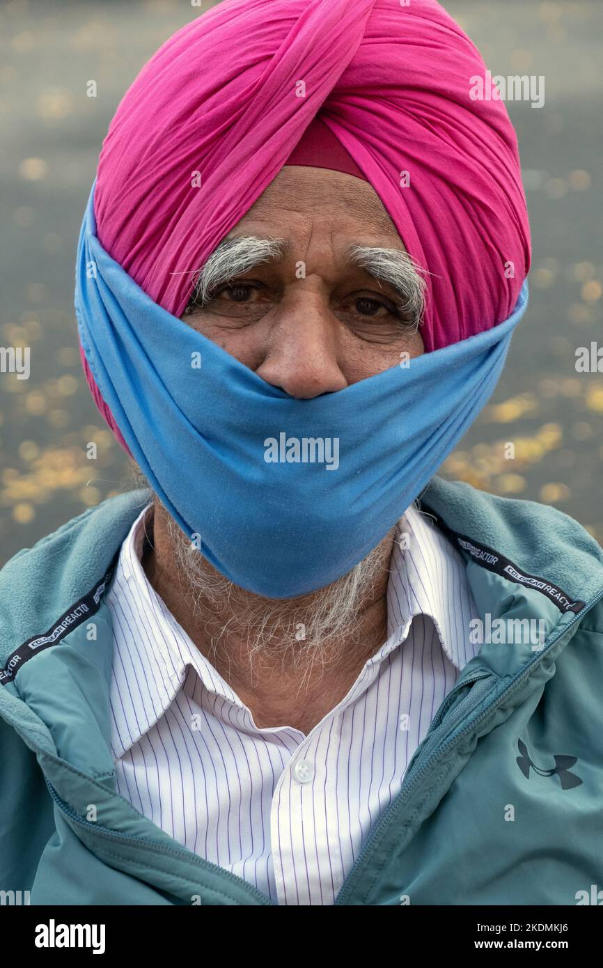 Posierte Porträt eines älteren Sikh-Mannes in einem rosa Turban und Teilmaske. An der 74. Street in Jackson Heights, Queens, New York City. Stockfoto