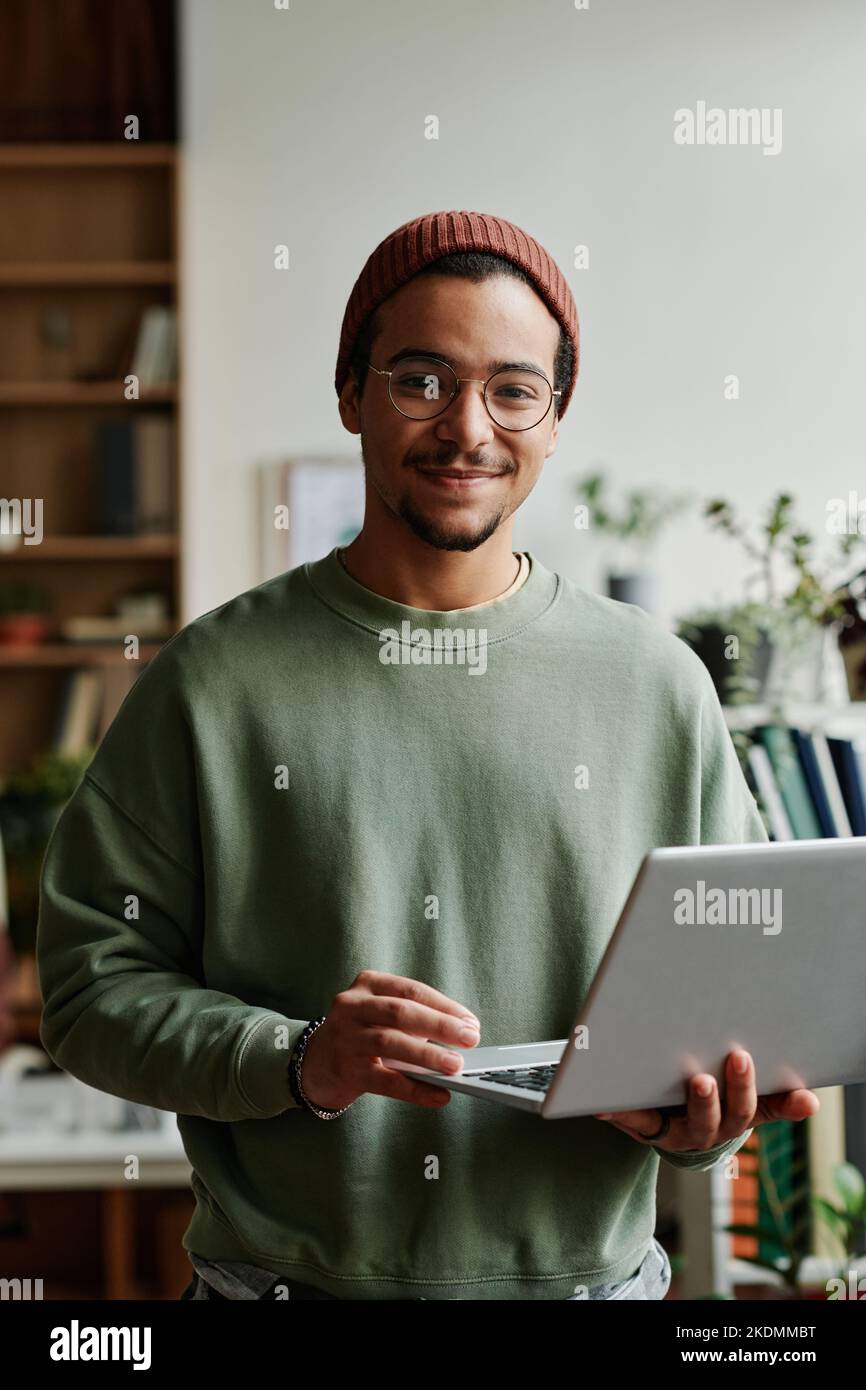 Junger, selbstbewusster IT-Techniker in der Freizeit schaut im Büro auf die Kamera, während er einen Laptop verwendet und mit Online- oder kodierten Daten arbeitet Stockfoto