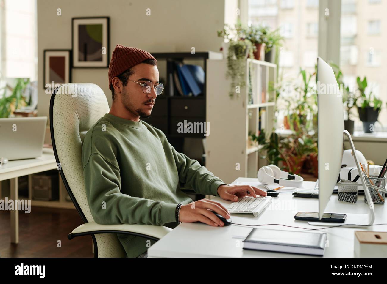 Junge seriöse IT-Support-Techniker, die den Computerbildschirm betrachten und die Maus anklicken, während sie am Arbeitsplatz neue Software bearbeiten Stockfoto