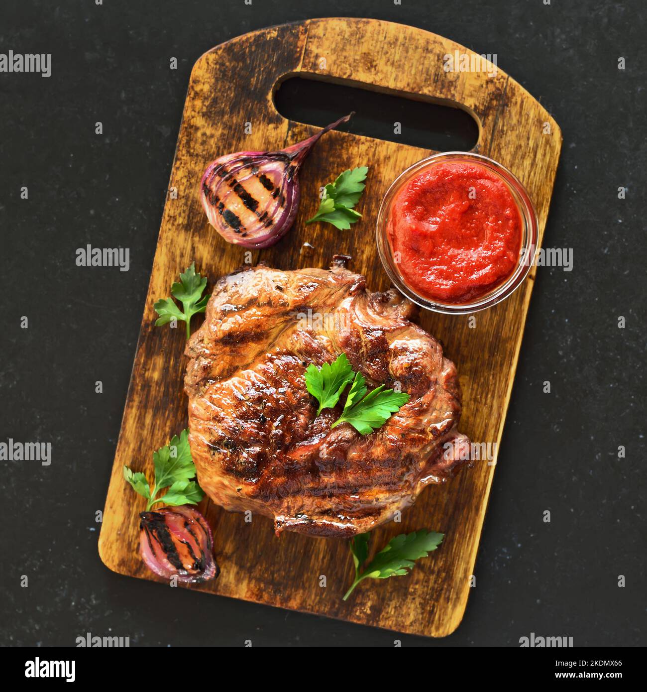 Gebratenes Rindersteak und Tomatensauce auf Schneidebrett über schwarzem Steintisch. Draufsicht, flach liegend Stockfoto