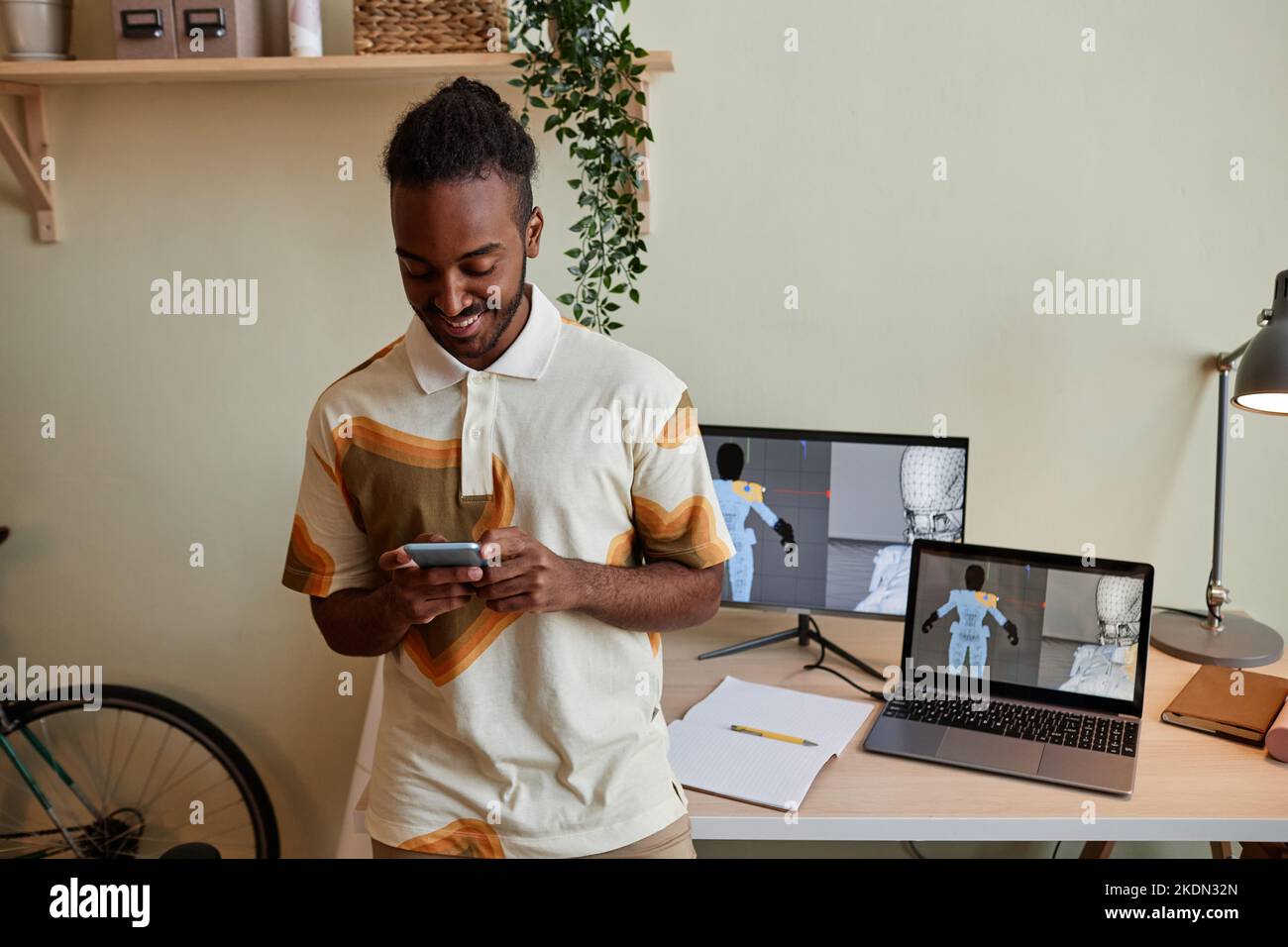 Waist-up-Porträt des kreativen schwarzen Mannes als digitaler 3D-Designer mit Smartphone nach Arbeitsplatz, Kopierraum Stockfoto