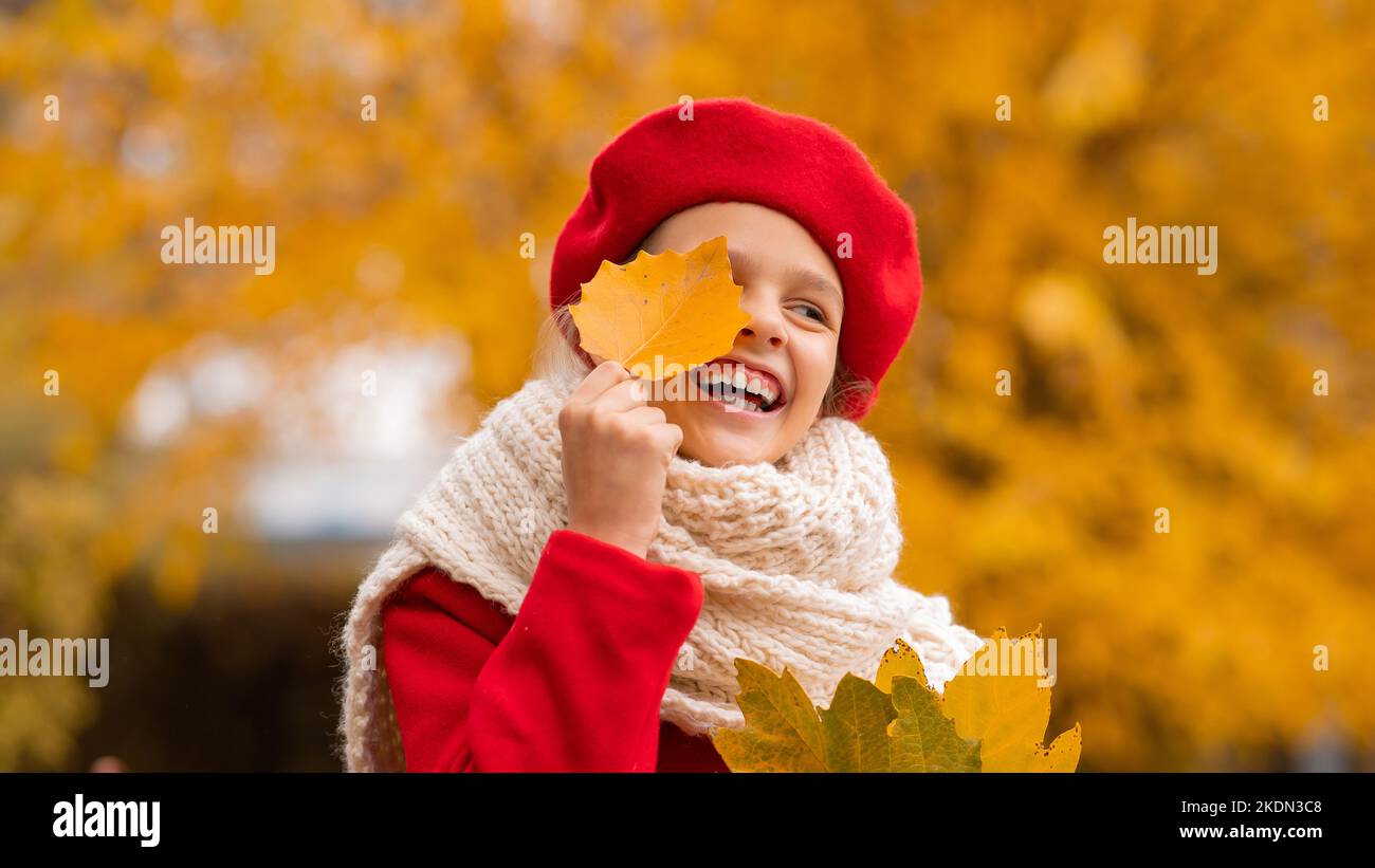 Glückliches kaukasisches Mädchen in einem roten Mantel und Baskenmütze spaziert im Herbst im Park. Stockfoto