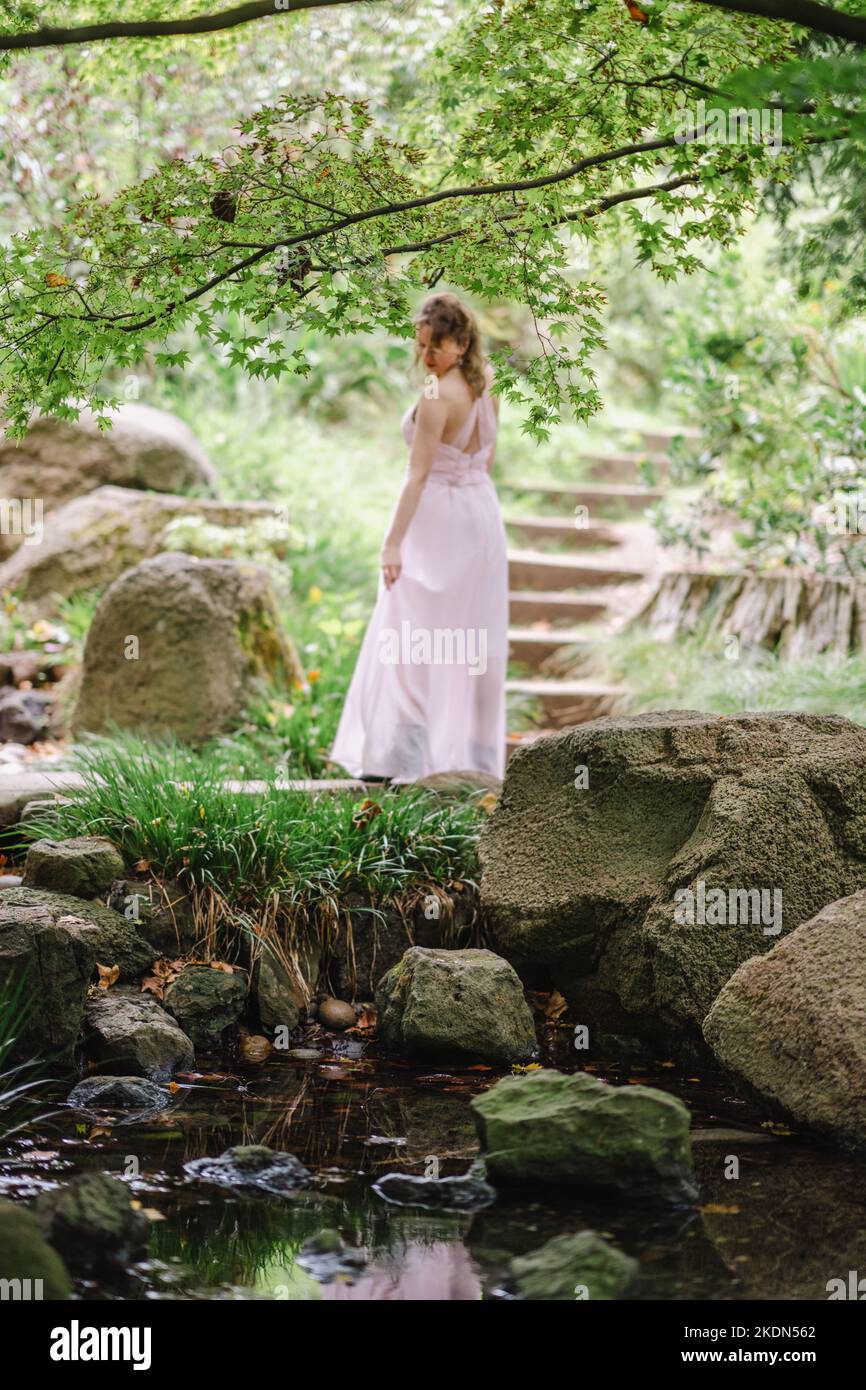 Frau im rosafarbenen Gown bei einem Besuch in einem idyllischen Garten Stockfoto