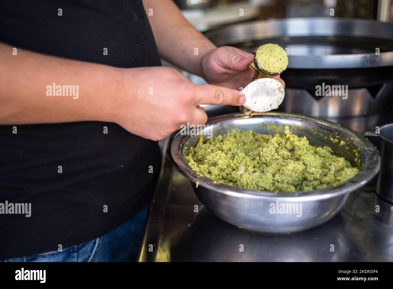 Mann Hände mit Werkzeug bilden Falafel Kugeln aus einer Edelstahlschale auf einer Arbeitsplatte in Close-Up Shot Stockfoto