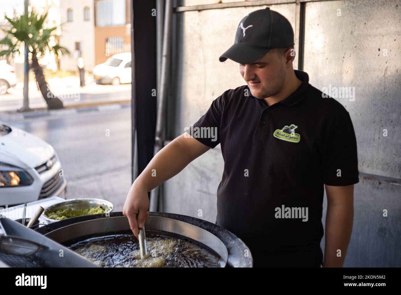 Ramallah, Ramallah und al-Bireh Governorate, Palästina - 22 2022. Juli: Ein lächelnder junger arabischer Mann kocht Falafel in einem großen Topf voller Öl Stockfoto