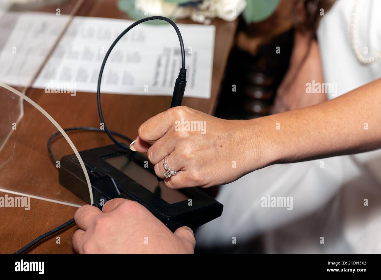 Der Hochzeitsfinger der Braut zeigt einen wunderschönen Diamantring, während sie ihre digitale Signatur für eine Heiratsurkunde offiziell unterschreibt. Stockfoto