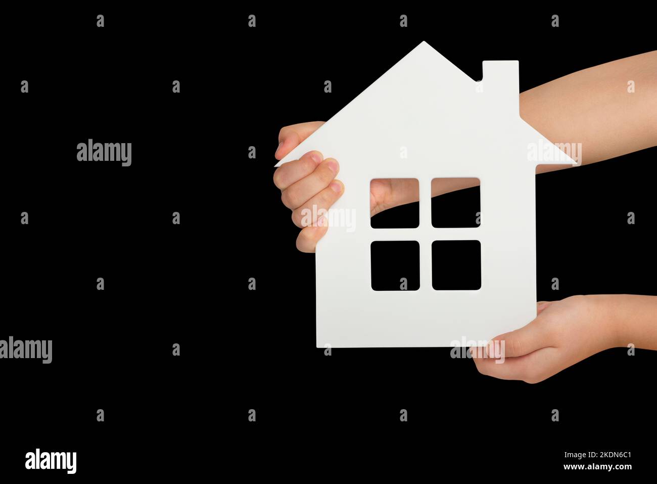 Haus in der Hand, Isolation. Weißes Modell eines Hauses in den Händen eines Kindes isoliert auf schwarzem Hintergrund. Obdachlosenheim, Familienheim, Hausversicherung Stockfoto